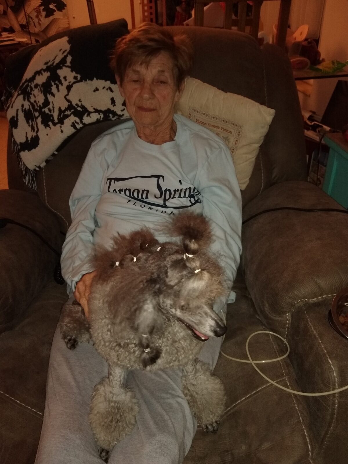 Woman holding a poodle with its fur styled in bows.