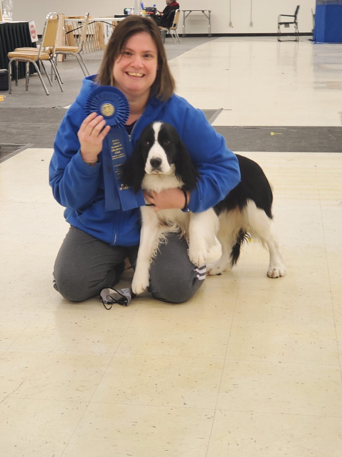 Woman in blue hoodie holding a blue ribbon with a black and white Springer Spaniel.