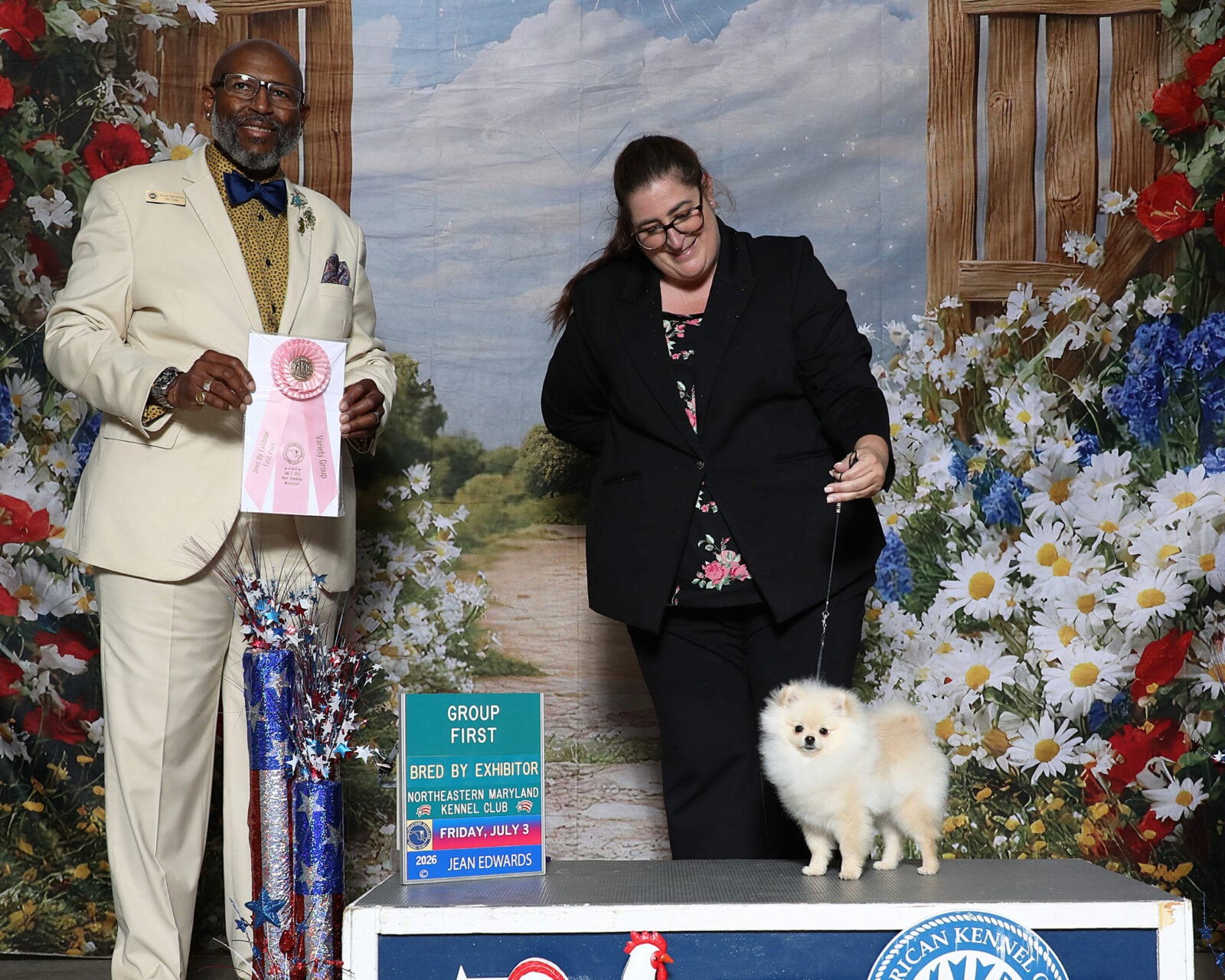 Man in suit holds ribbon, woman with Pomeranian dog on stage.