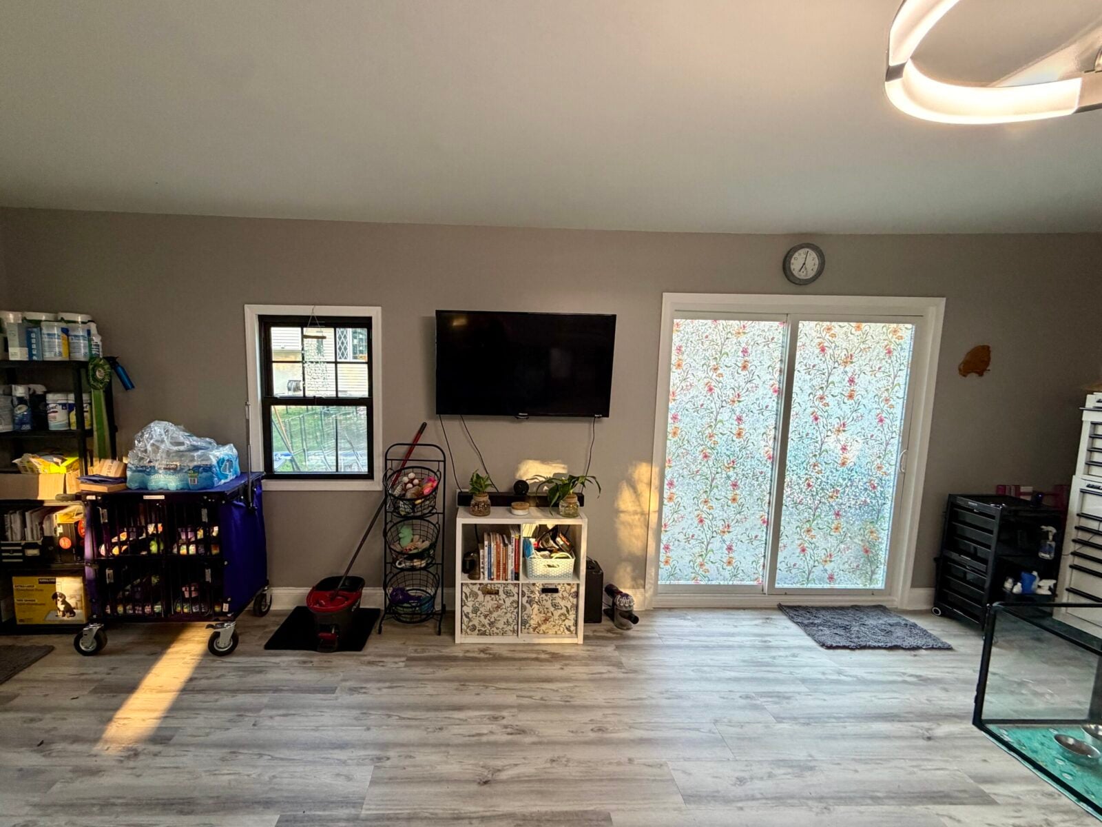 Living room with TV, window, sliding glass door with floral film, and storage shelves.