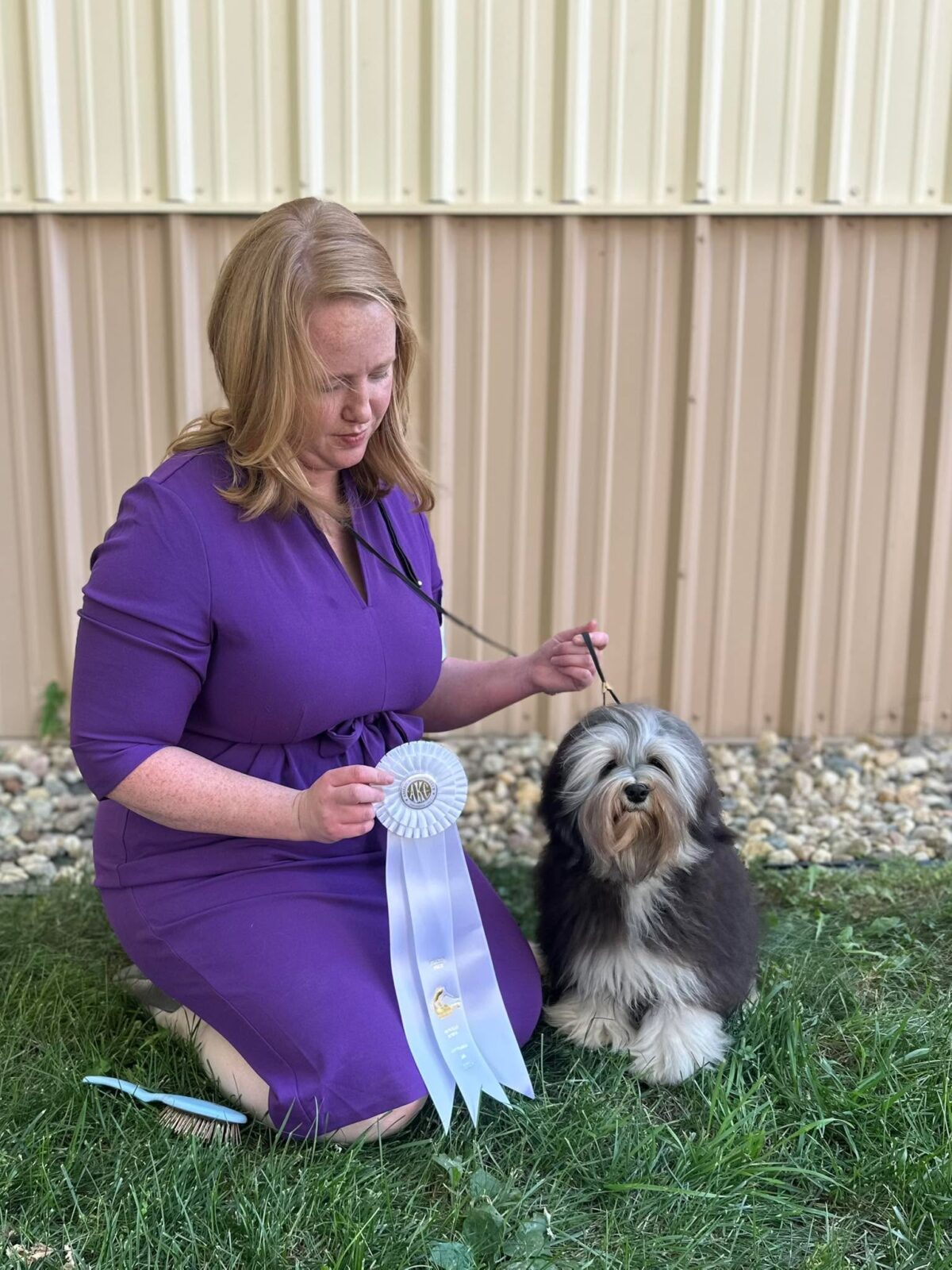Woman in purple dress with award ribbon next to a fluffy dog.