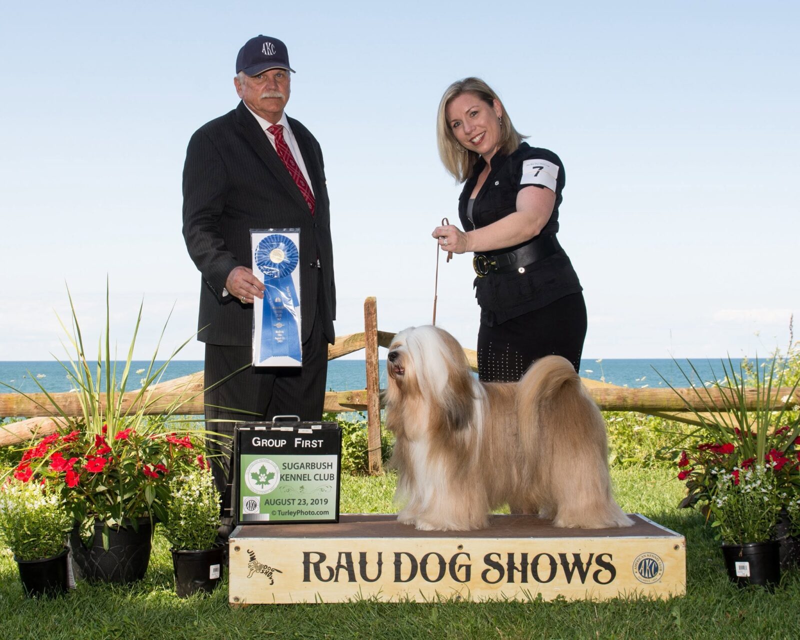 Dog show winner with handler and judge, holding blue ribbon.