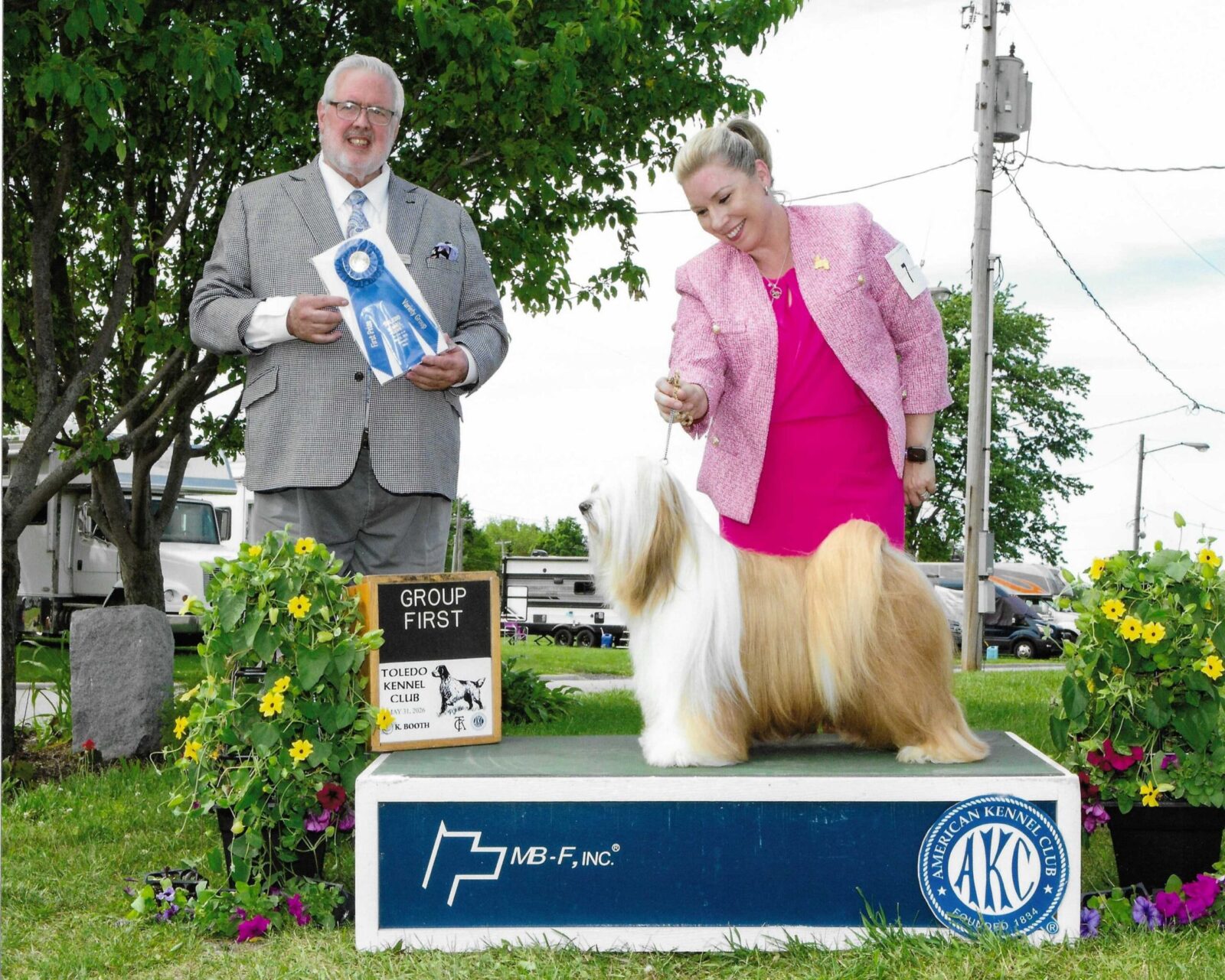 Man and woman with award-winning Lhasa Apso on a podium.