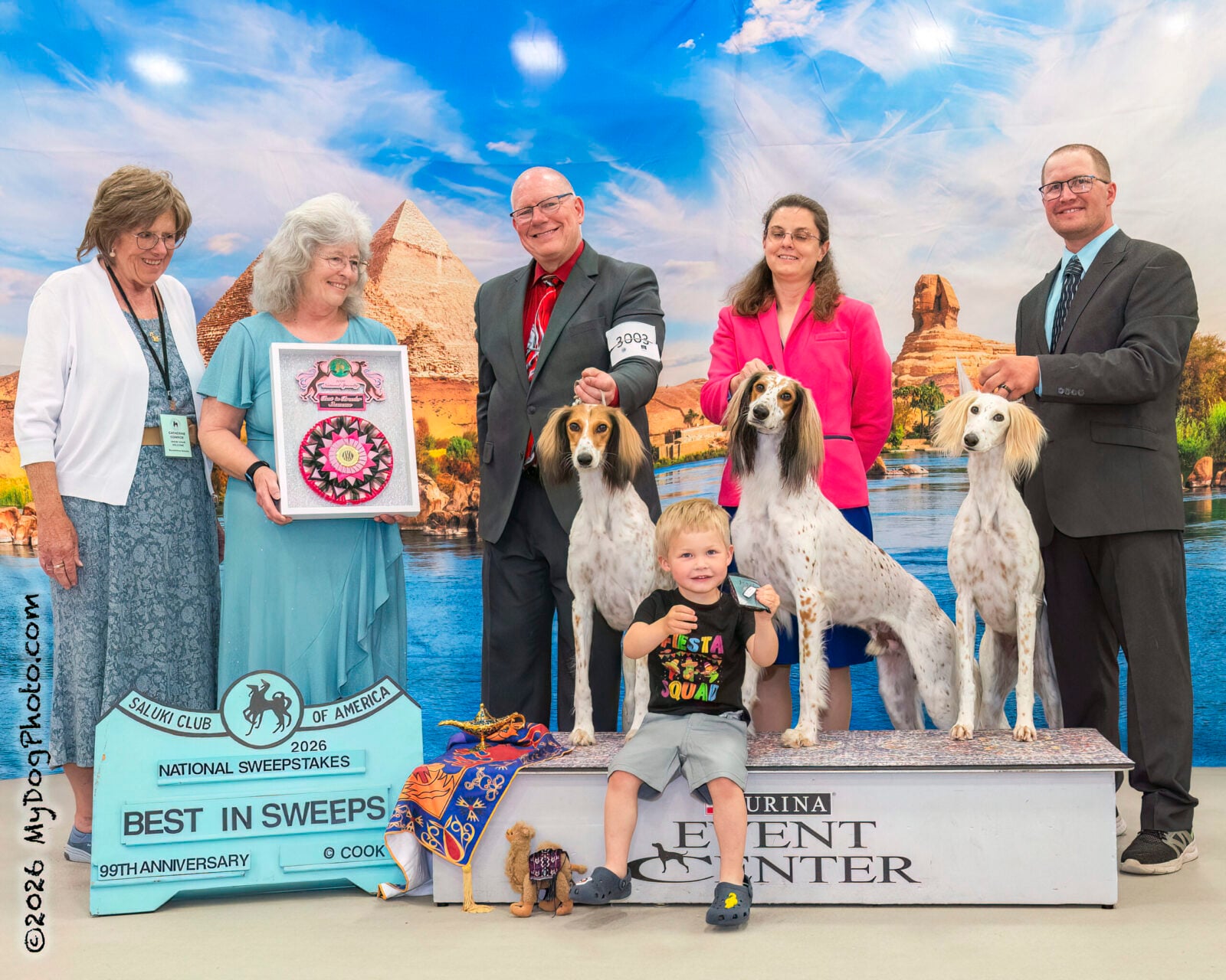 People and three Saluki dogs with a "Best in Sweeps" award and Egyptian backdrop.