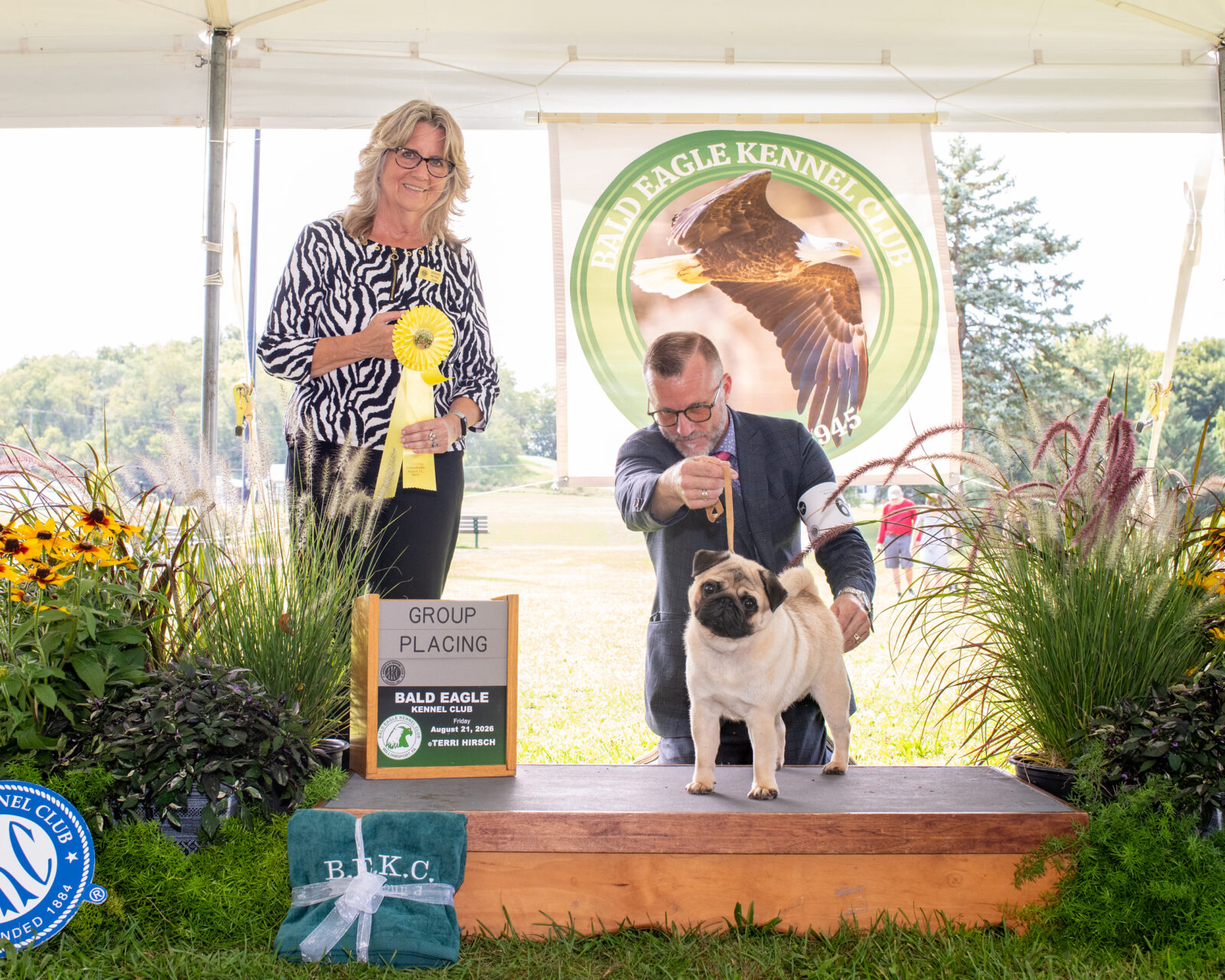 Man with pug on podium, woman with ribbon, Bald Eagle Kennel Club banner.